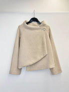 A beige textured knit sweater with a high mock neck and asymmetrical draped front detail, hanging on a black hanger against a plain white wall.
