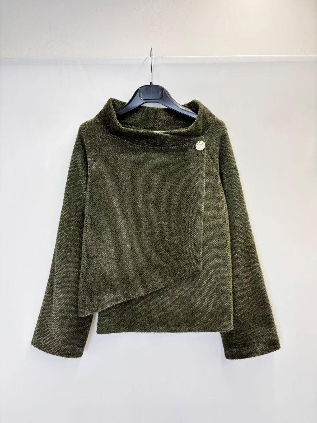 An olive green textured knit wrap jacket with a high mock neck and asymmetrical draped front, hanging on a black hanger against a plain white wall.