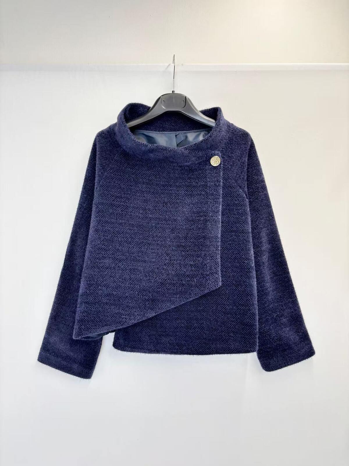 A navy blue textured knit wrap jacket with a single button closure, hanging on a black hanger against a plain white wall.