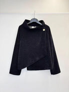 A black textured wrap-style jacket with a high mock neck and asymmetrical button closure, hanging on a black hanger against a plain white wall.