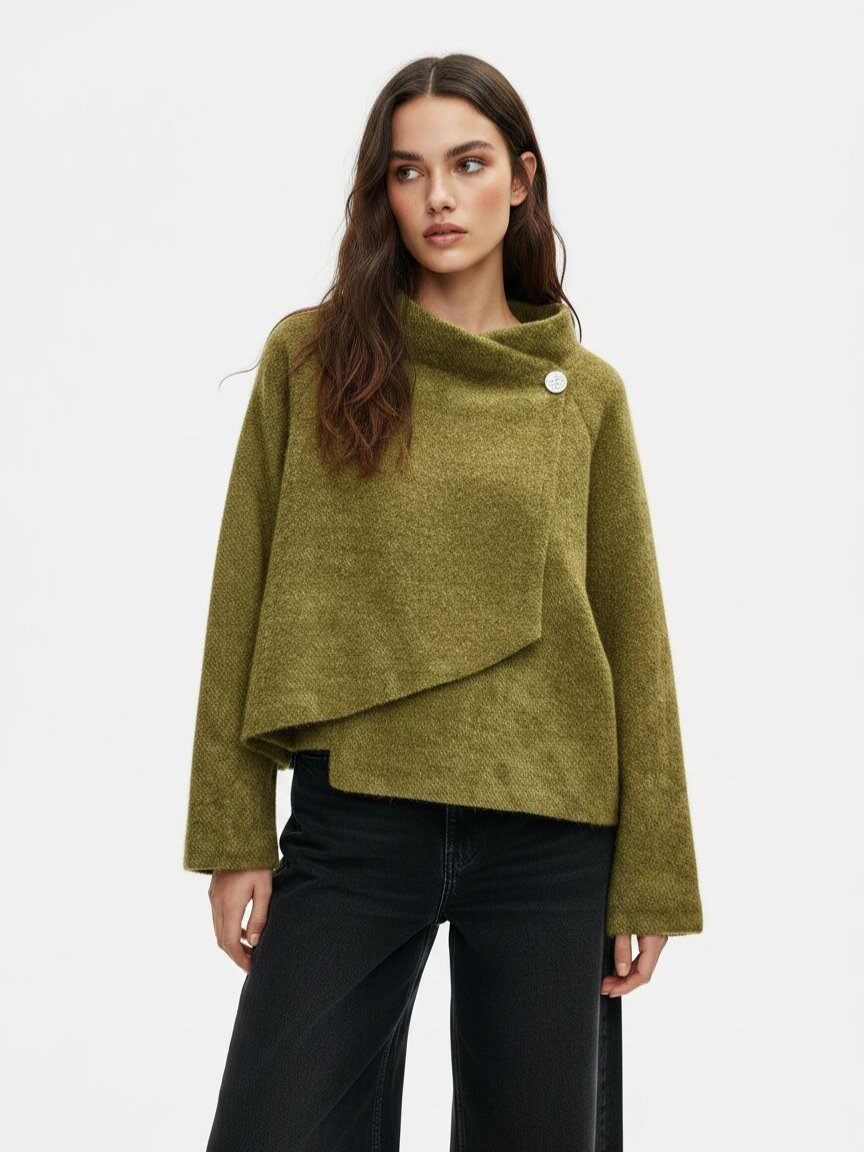 A woman wearing a textured olive green asymmetrical wrap sweater with a single decorative button, paired with black wide-leg jeans, against a plain white studio background.