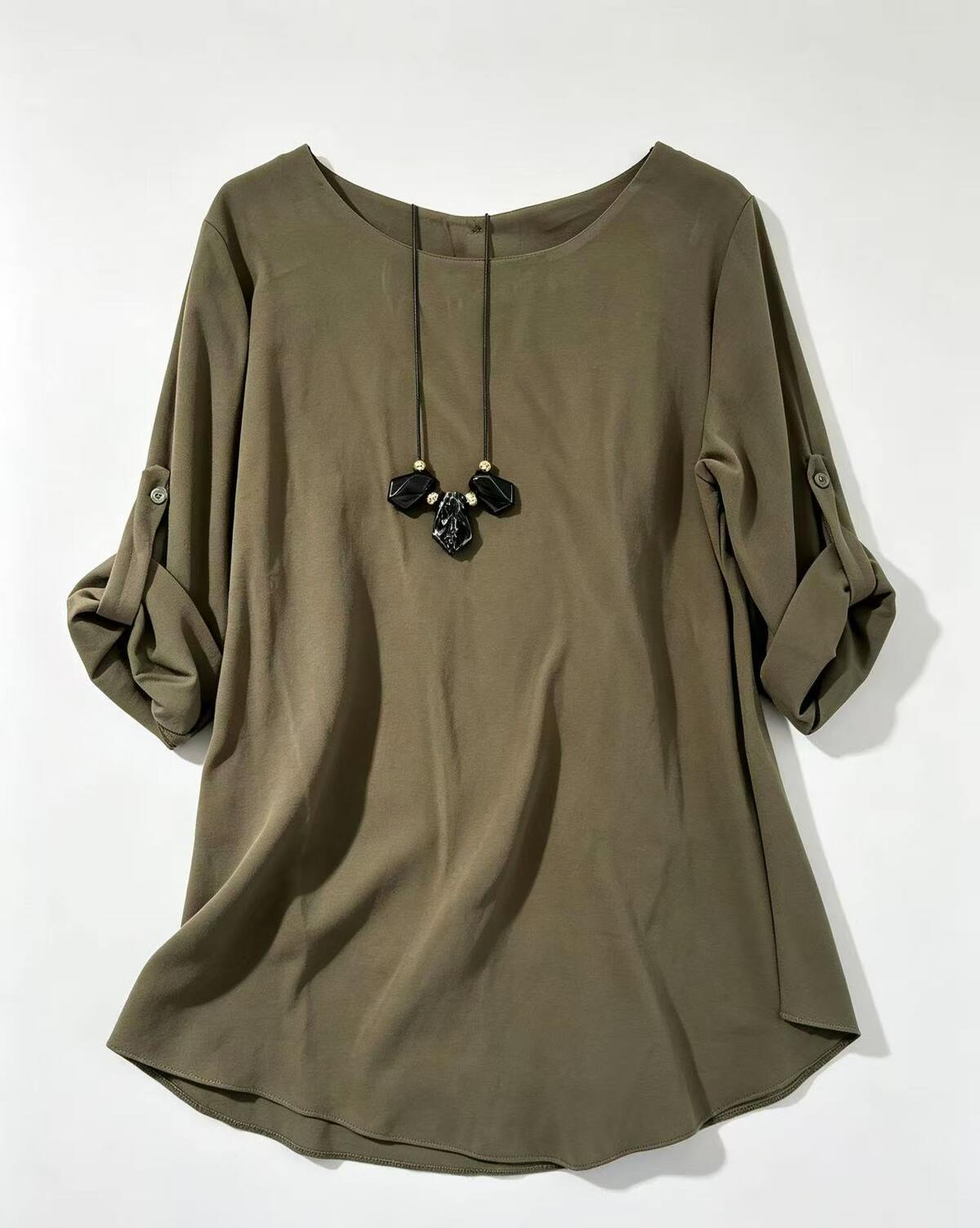 An olive green long-sleeve top with rolled-up sleeves featuring button details, shown with a black beaded necklace on a plain white background.