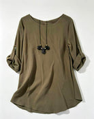 An olive green long-sleeve top with rolled-up sleeves featuring button details, shown with a black beaded necklace on a plain white background.