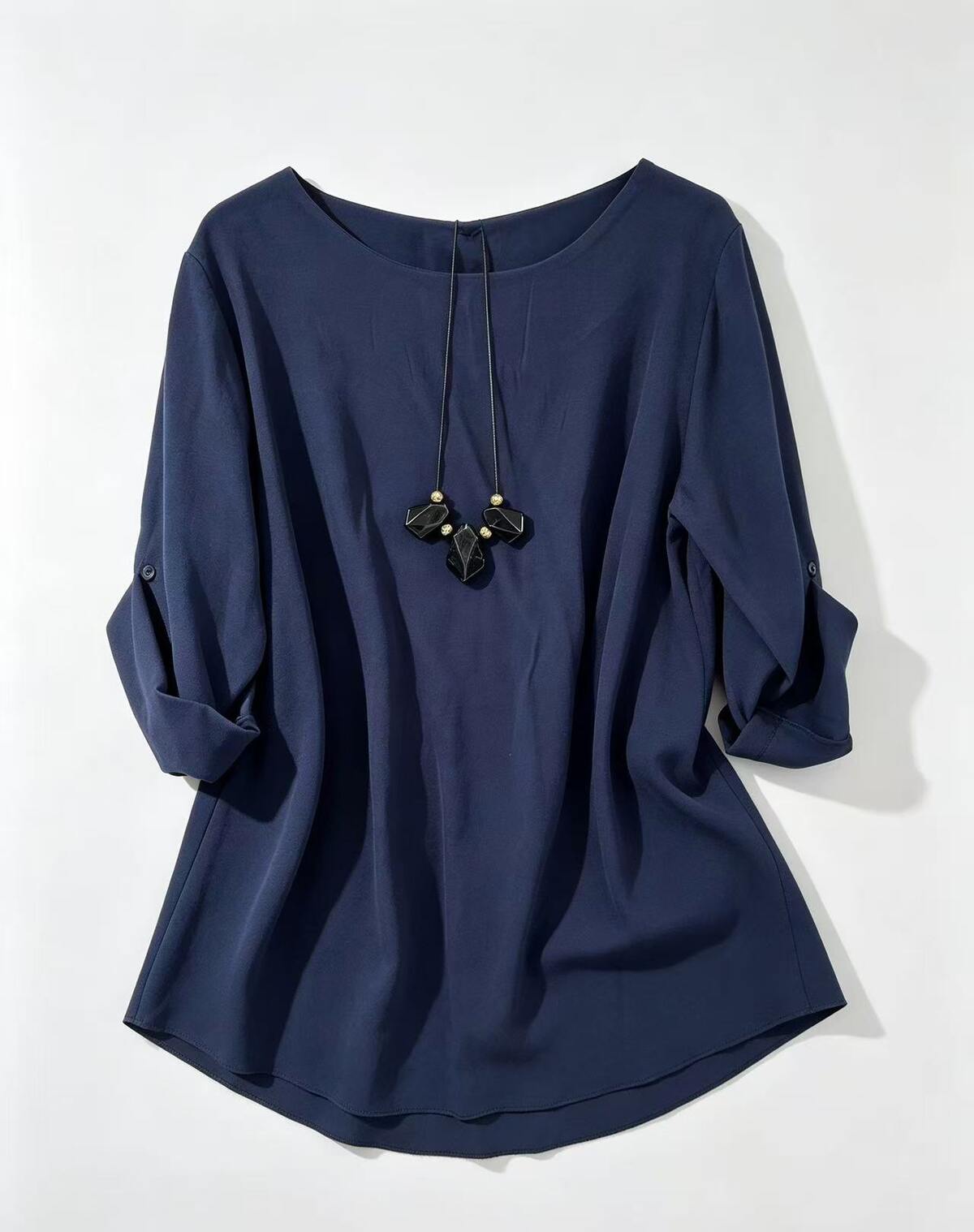 A navy blue long-sleeve top with a wide round neckline, three-quarter sleeves rolled up to the forearms, and a drawstring detail at the collar, displayed on a light gray background.