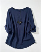 A navy blue long-sleeve top with a wide round neckline, three-quarter sleeves rolled up to the forearms, and a drawstring detail at the collar, displayed on a light gray background.