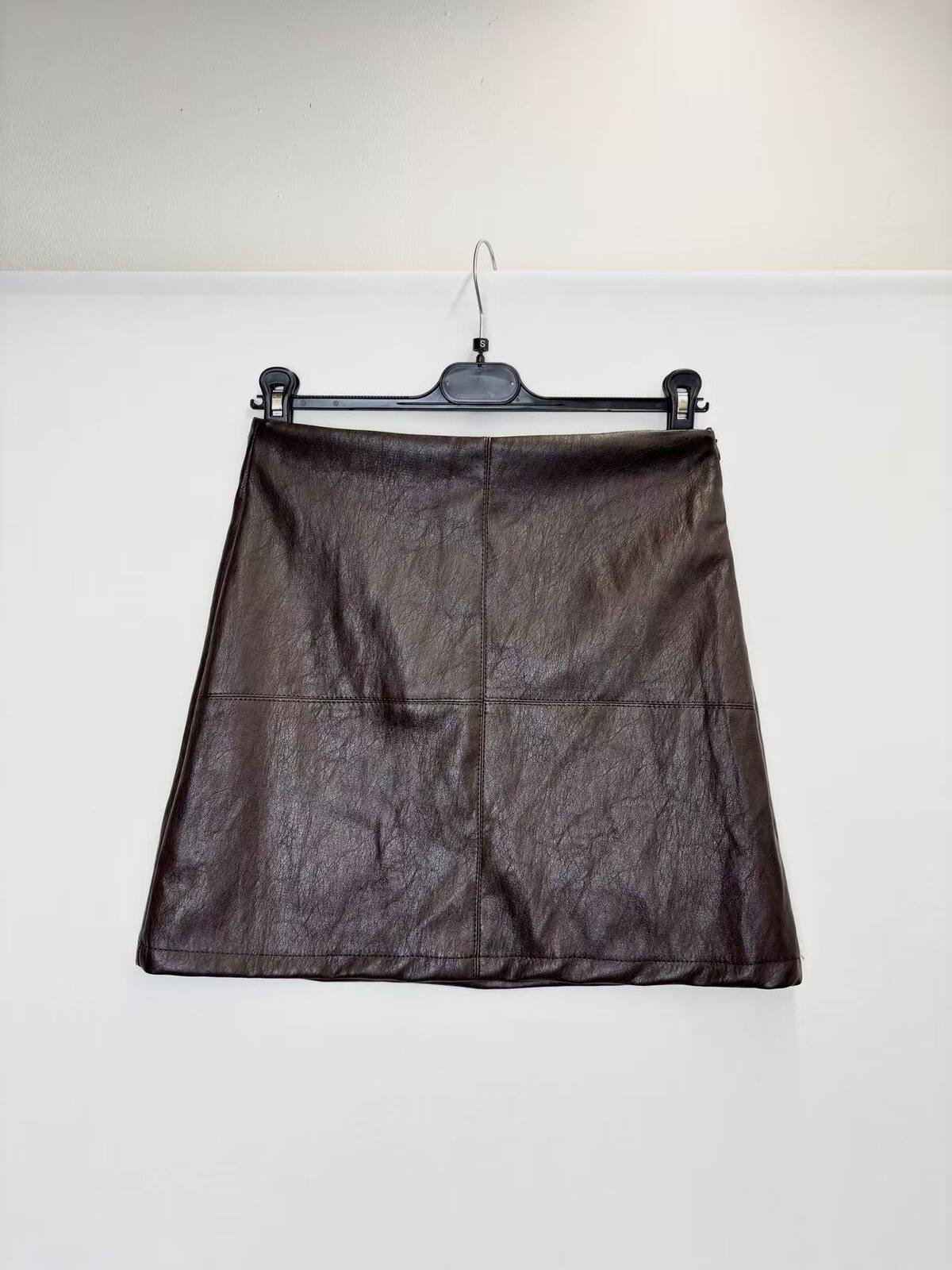 A dark brown faux-leather A-line mini skirt with a crinkled texture, hanging on a black hanger against a plain white wall.