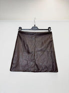 A dark brown faux-leather A-line mini skirt with a crinkled texture, hanging on a black hanger against a plain white wall.