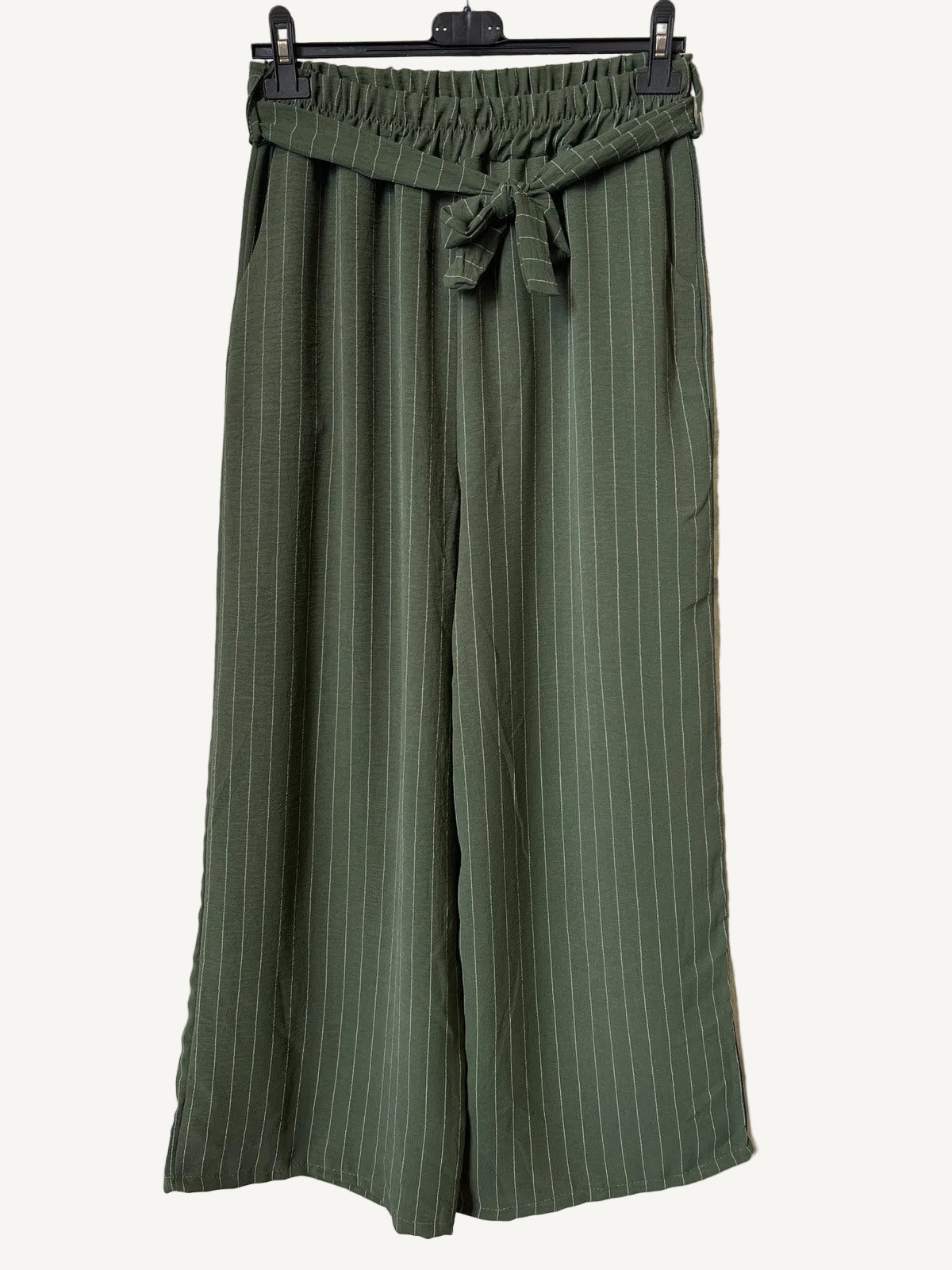 Green striped pants hanging on a rack against a textured white background
