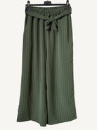 Green striped pants hanging on a rack against a textured white background