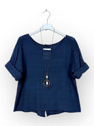 A dark navy blue short-sleeve top with rolled cuffs, hanging on a white hanger with a long pendant necklace draped over it, against a plain white background.