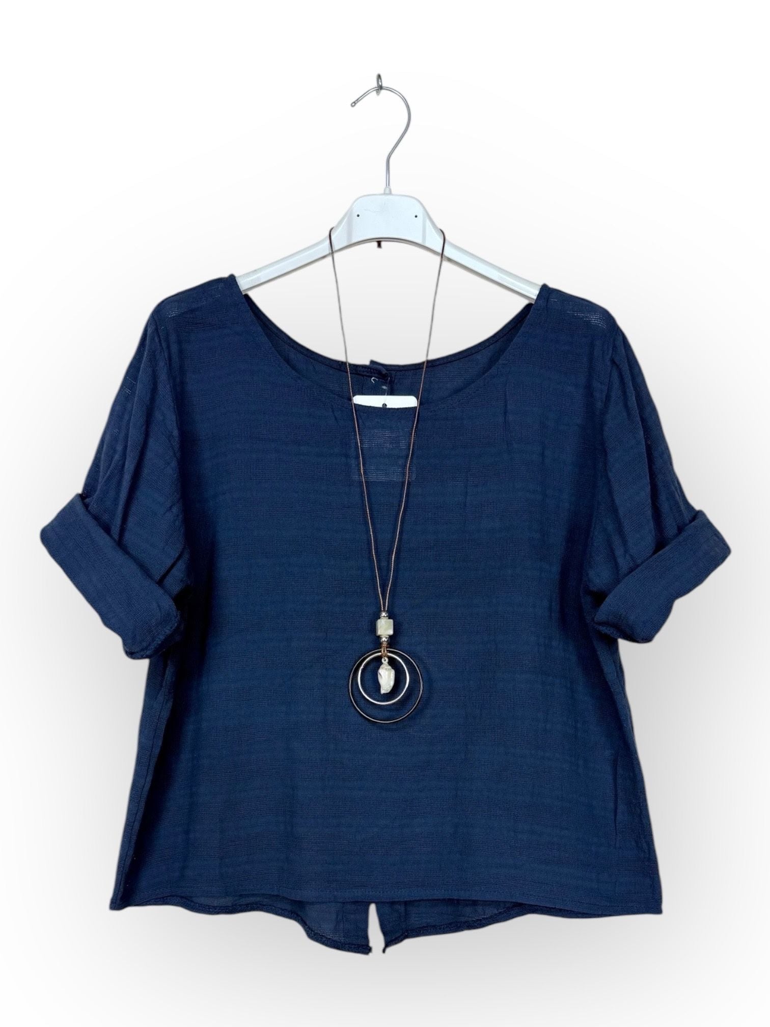 A dark navy blue short-sleeve top with rolled cuffs, hanging on a white hanger with a long pendant necklace draped over it, against a plain white background.