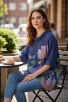 Woman sitting outdoors at a cafe wearing a blue floral-patterned tunic top