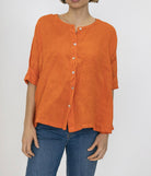 Person wearing an orange button-up shirt and blue jeans on a plain background