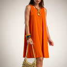 A woman wearing a sleeveless bright orange A-line dress, holding a woven straw bag