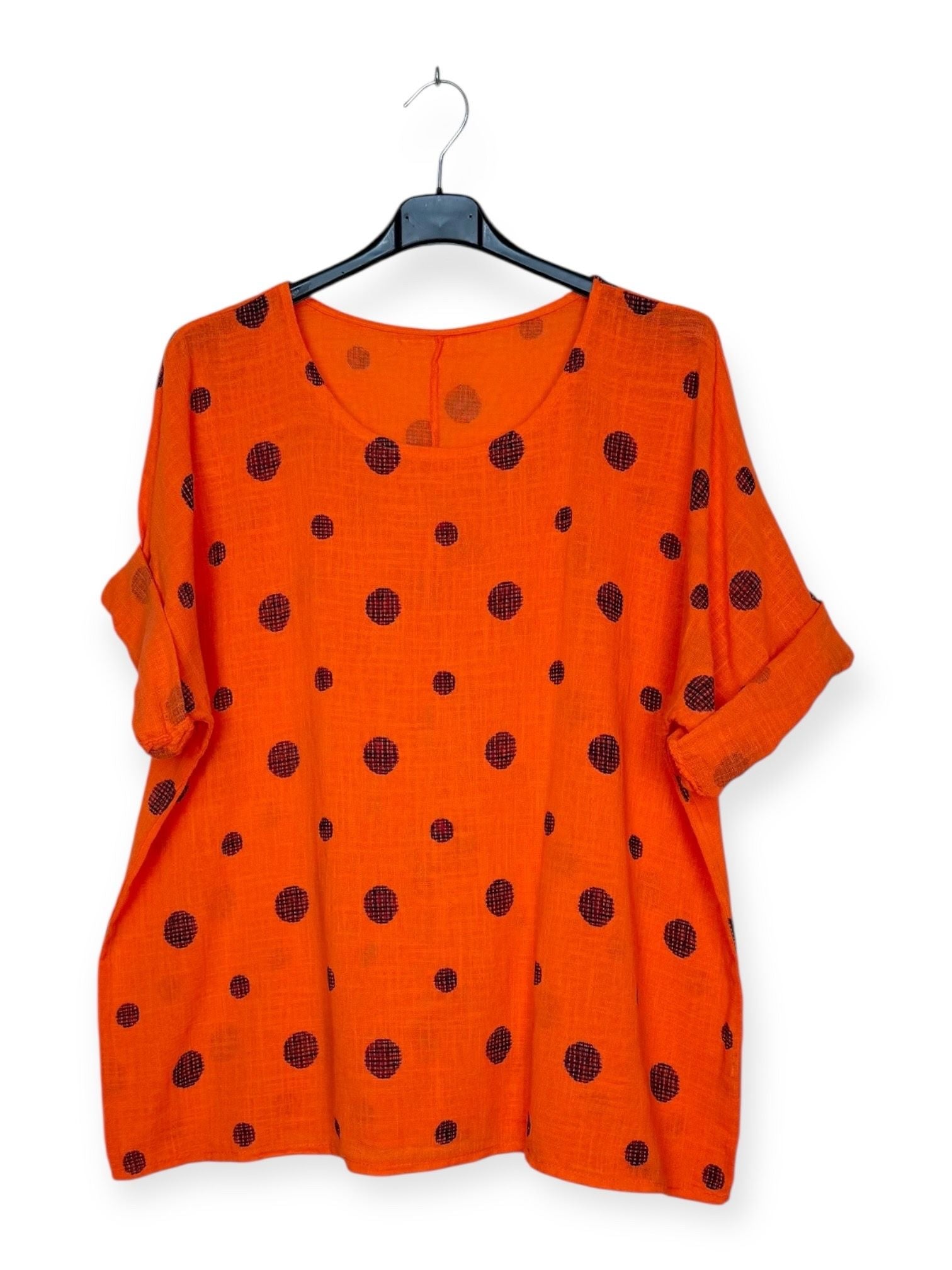 Orange top with black polka dots on a hanger against a white background