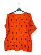 Orange top with black polka dots on a hanger against a white background