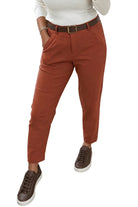 A person wearing rust-colored cropped trousers with a dark brown belt, a white long-sleeve top, and brown sneakers