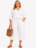 Woman wearing a white outfit with wide-leg pants and a straw bag on a white background