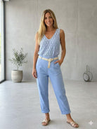 Woman wearing a light blue sleeveless top and pants in a minimalistic room.