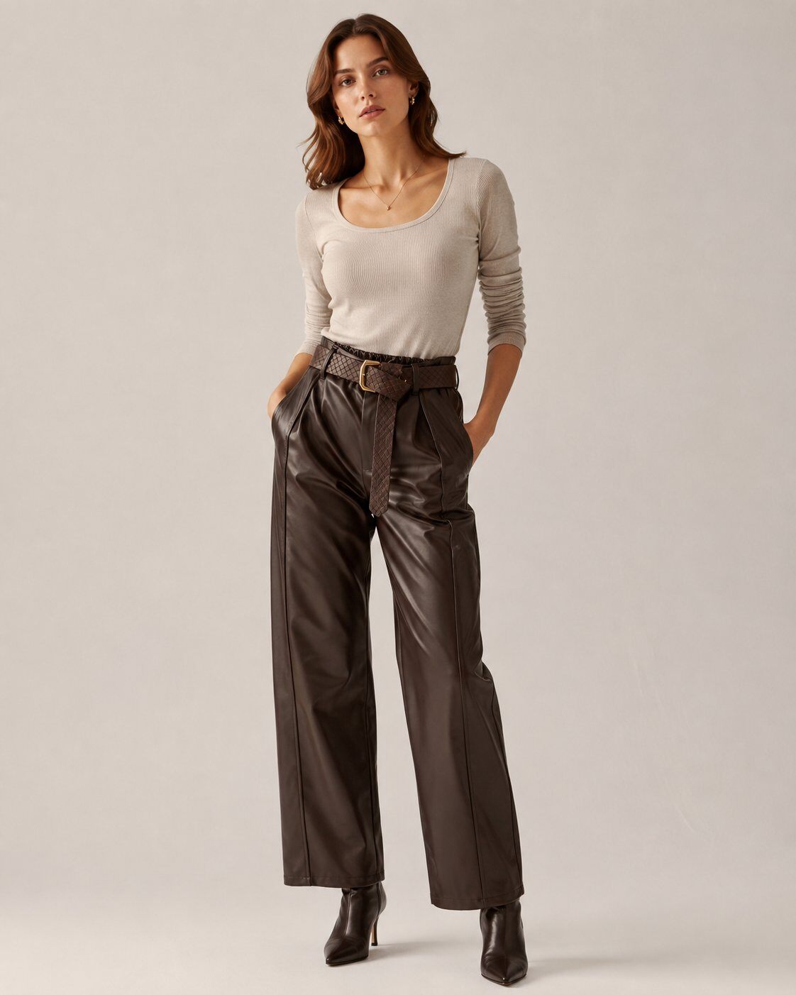 A woman modeling a beige long-sleeve scoop-neck top and dark brown wide-leg faux-leather trousers with a matching belt, paired with black ankle boots