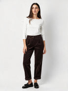 A woman modeling a white long-sleeve top and dark brown corduroy trousers with black loafers
