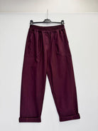 A pair of dark burgundy wide-leg pants with an elastic waistband, hanging from a black hanger against a plain white wall.