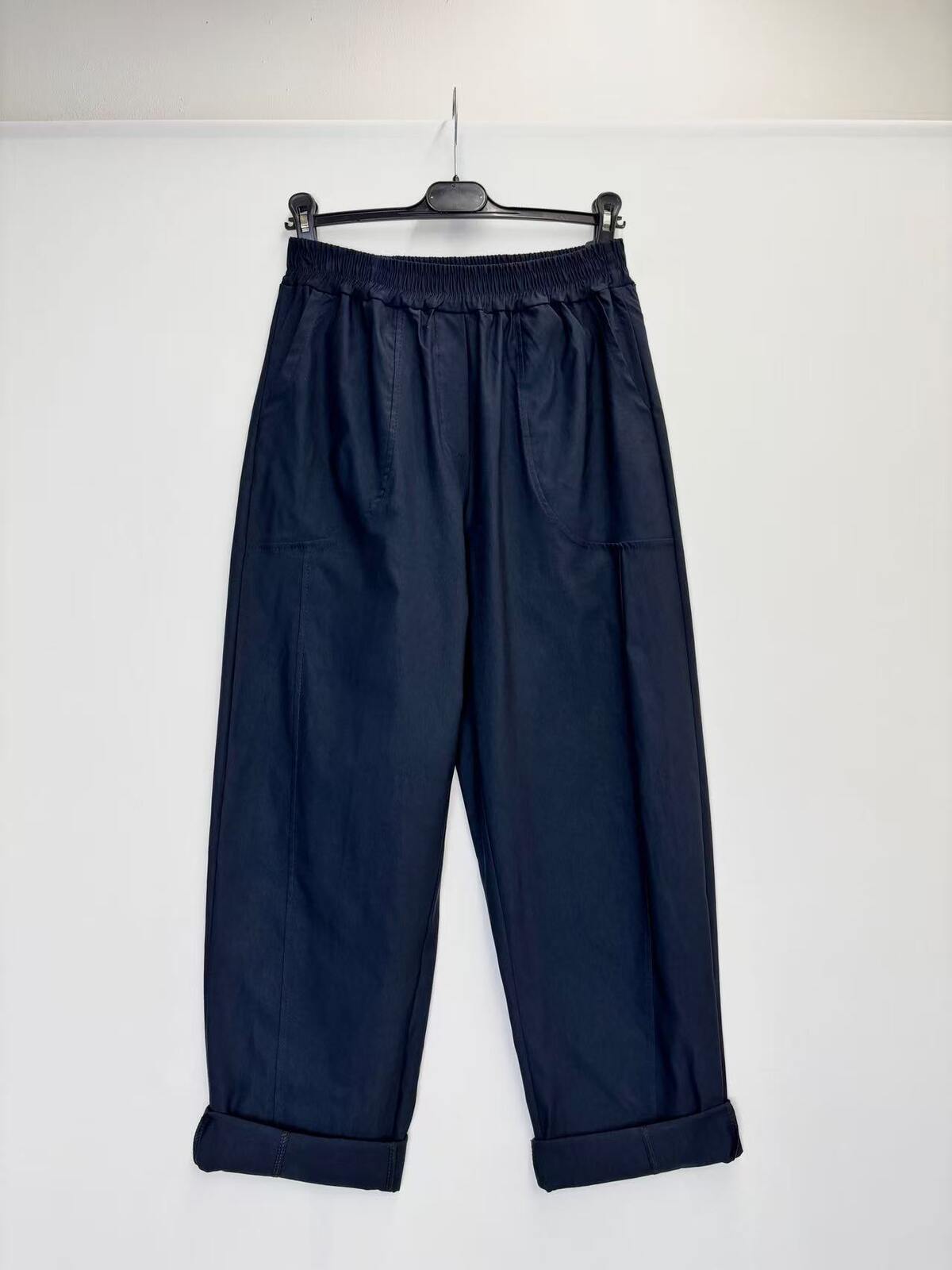 A pair of dark navy blue cropped pants with an elastic waistband and rolled cuffs, hanging on a black hanger against a plain white wall.