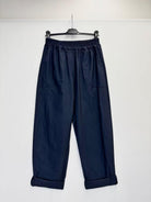 A pair of dark navy blue cropped pants with an elastic waistband and rolled cuffs, hanging on a black hanger against a plain white wall.