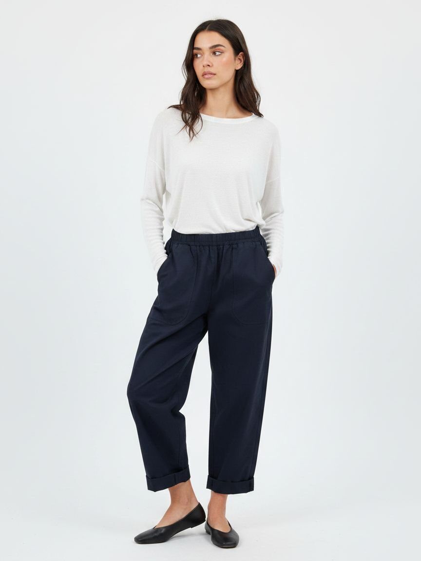 A woman modeling a pair of dark navy wide-leg cropped trousers with a drawstring waist, paired with a white long-sleeve top and black flats, against a plain white studio background.