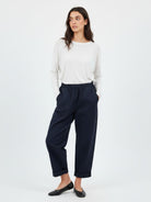 A woman modeling a pair of dark navy wide-leg cropped trousers with a drawstring waist, paired with a white long-sleeve top and black flats, against a plain white studio background.