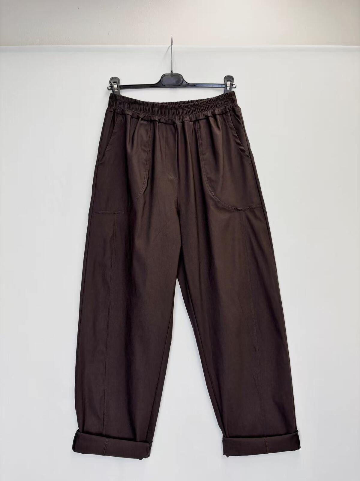 Dark brown wide-leg pants with an elastic waistband and cuffed hems, hanging on a black hanger against a plain white wall.