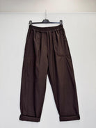 Dark brown wide-leg pants with an elastic waistband and cuffed hems, hanging on a black hanger against a plain white wall.