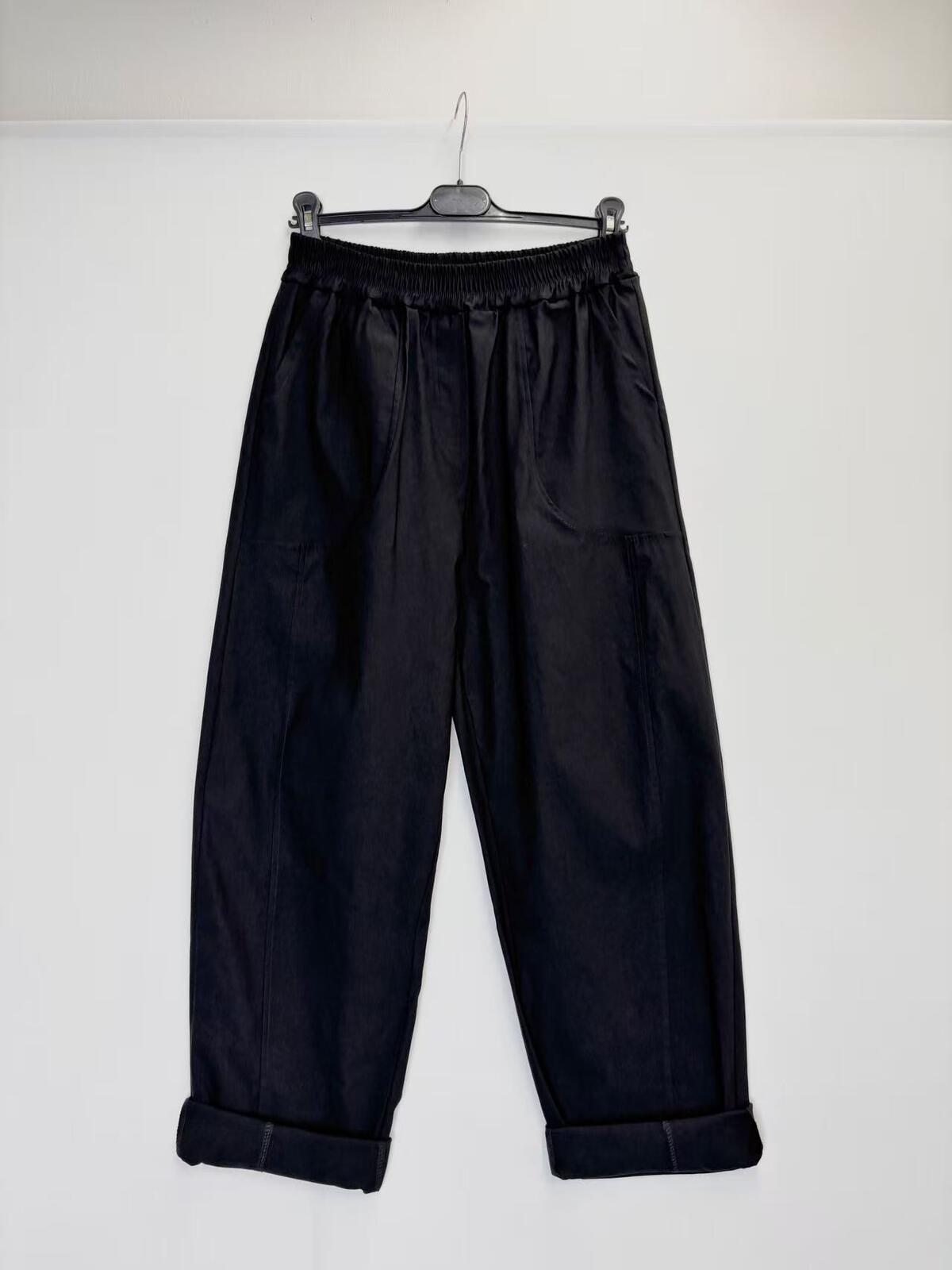 Black wide-leg cropped pants with an elastic waistband and rolled cuffs, hanging on a black hanger against a plain white wall.