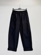 Black wide-leg cropped pants with an elastic waistband and rolled cuffs, hanging on a black hanger against a plain white wall.