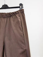 Brown wide-leg trousers with an elastic waistband, hanging on a black hanger against a plain white wall.
