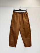 A pair of brown wide-leg cropped pants with an elastic waistband, hanging from a black hanger against a plain white backdrop.