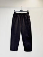 Black wide-leg cropped pants with an elastic waistband, hanging on a black hanger against a plain white wall.