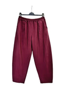 A pair of loose-fitting, pleated trousers in a deep burgundy or maroon color, hanging from a black hanger against a plain white backdrop.