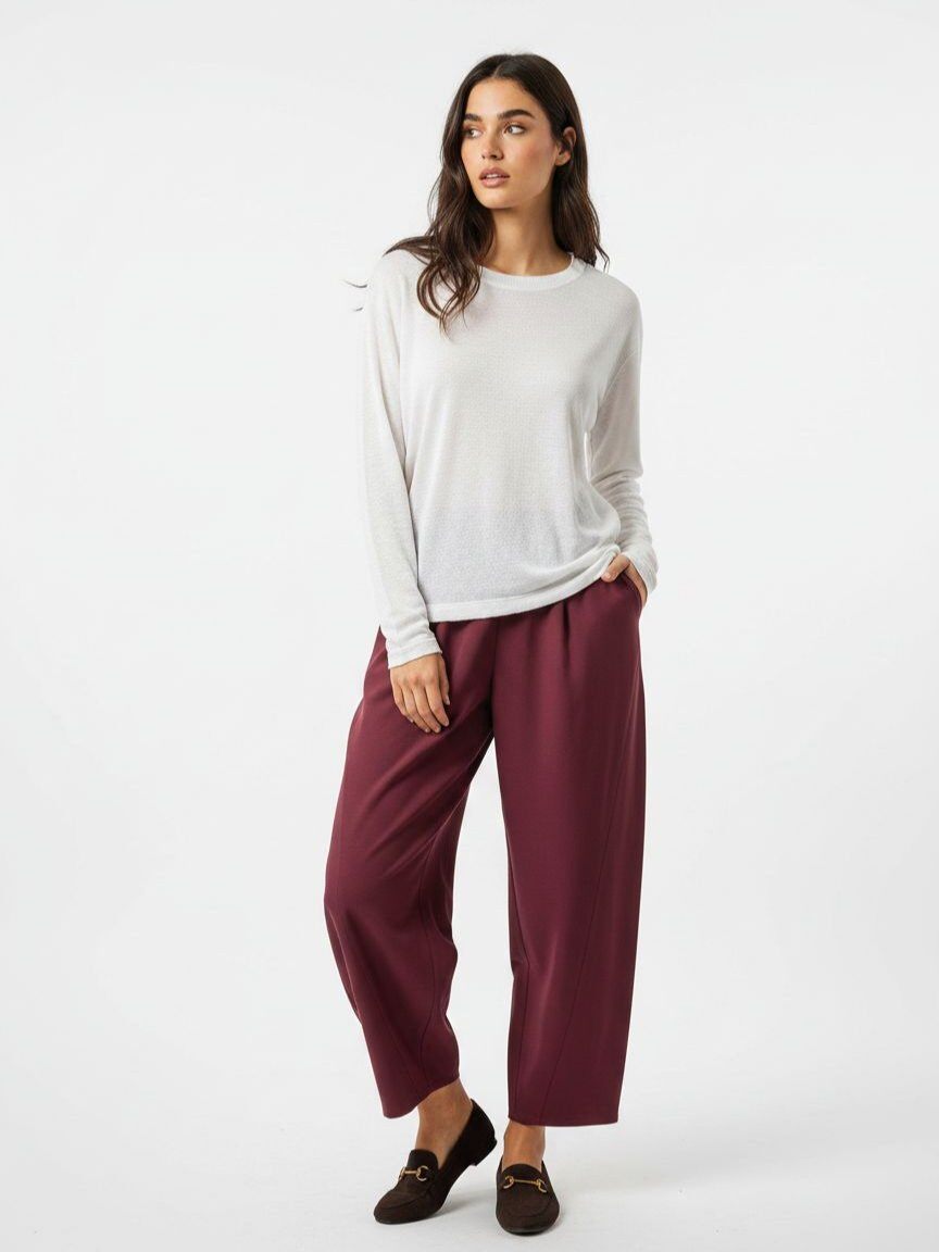A woman modeling a white long-sleeve knit top and wide-leg burgundy cropped pants with dark loafers, photographed against a clean white studio background.