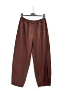 A pair of brown wide-leg cropped pants with an elastic waistband, hanging on a black hanger against a plain white wall.