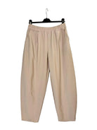 A pair of beige wide-leg cropped pants with an elastic waistband, hanging on a black hanger against a plain off-white wall.