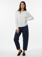 A woman modeling a white long-sleeve crewneck top and navy blue cropped trousers, paired with dark brown loafers, against a plain white studio background.