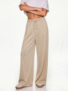 A model wearing beige wide-leg lounge pants with an elastic drawstring waist