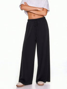 A model wearing black wide-leg drawstring pants, styled with a white cropped t-shirt and beige slip-on shoes, against a plain white background.