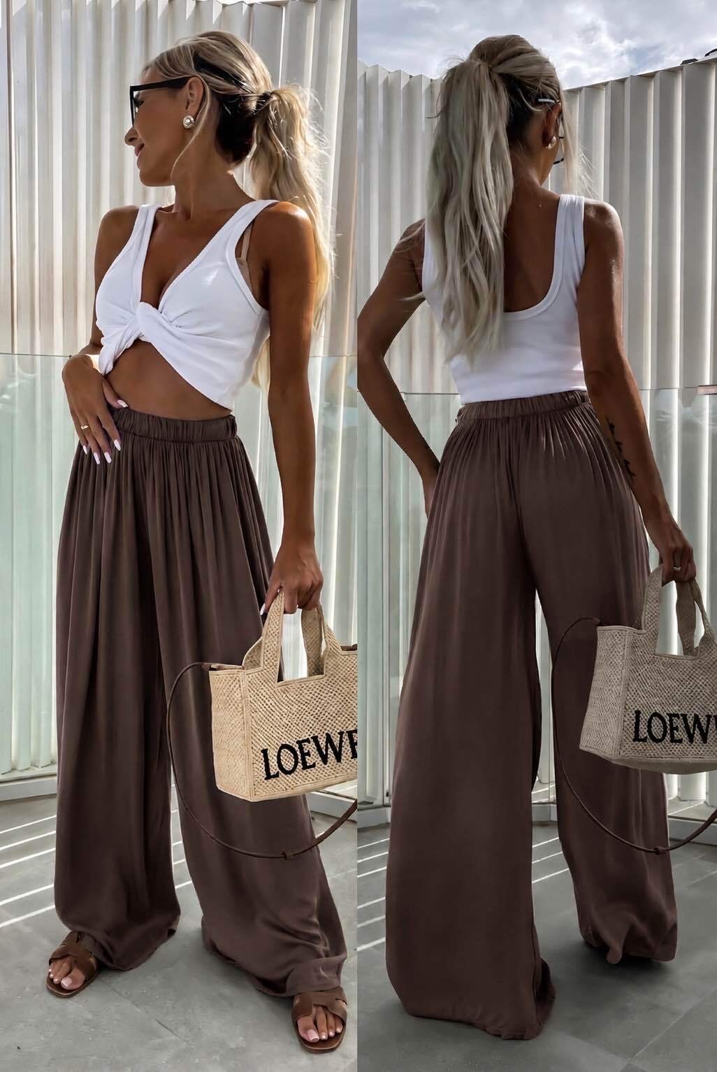 Woman wearing a white top and brown wide-leg pants, holding a Loewe bag.