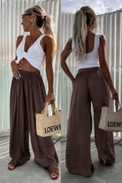 Woman wearing a white top and brown wide-leg pants, holding a Loewe bag.