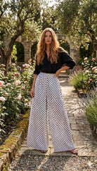 Woman in a black top and white polka dot pants standing in a garden.