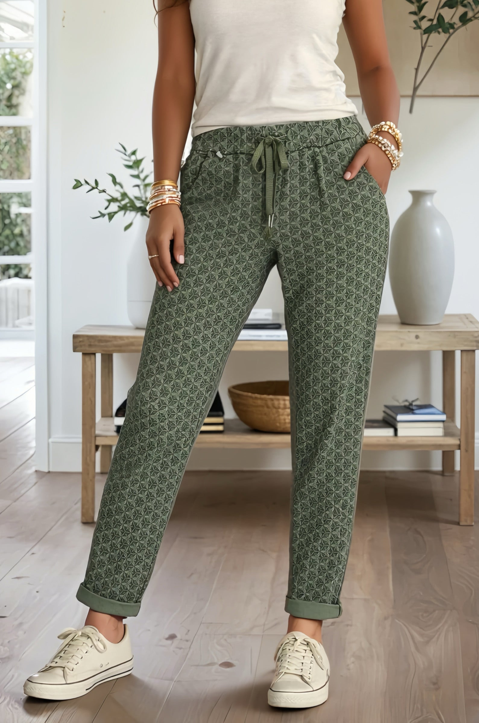 Person wearing green patterned pants with a white top and sneakers in a home setting.