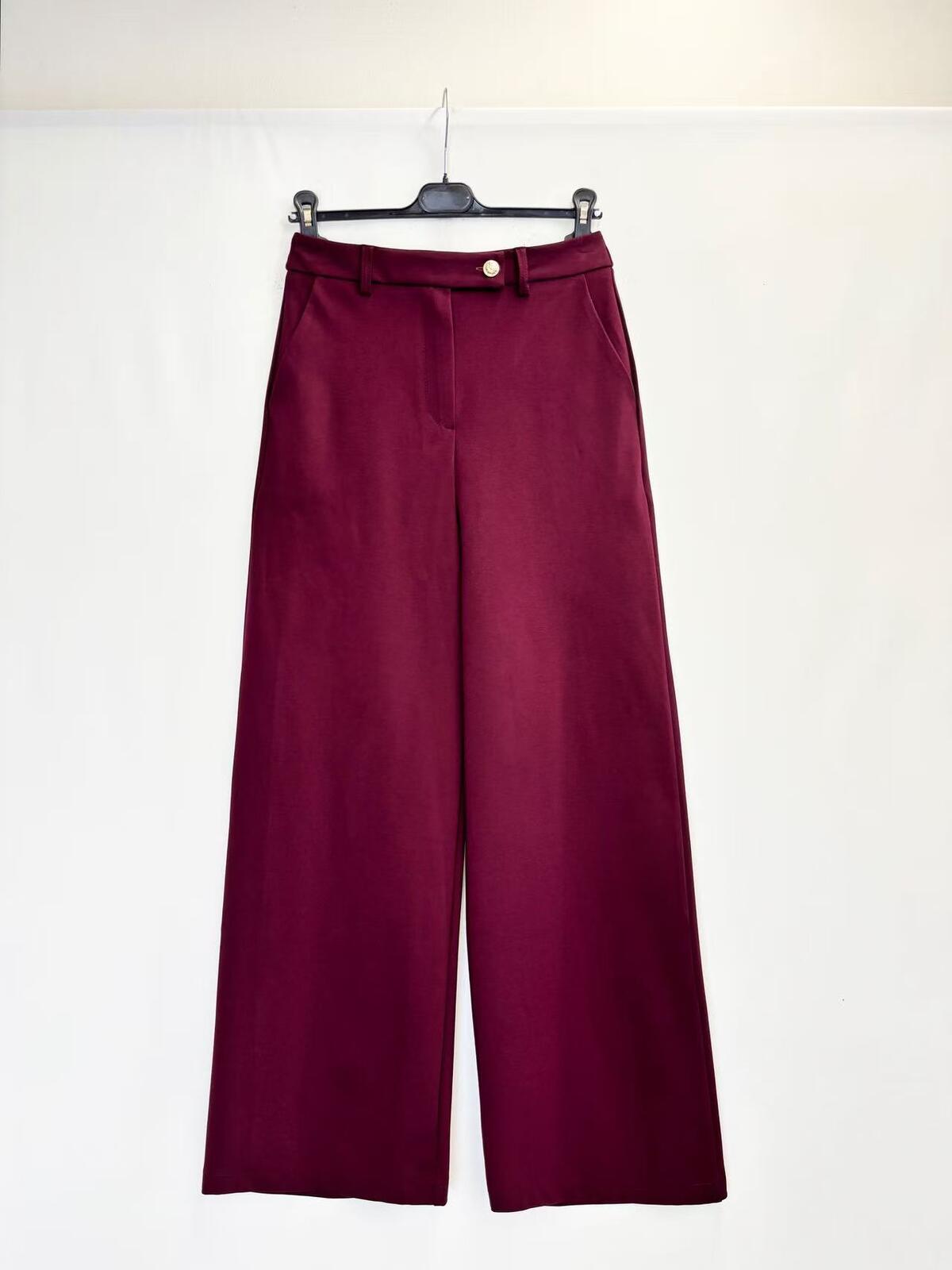A pair of wide-leg trousers in deep burgundy, hanging on a black hanger against a plain white backdrop.