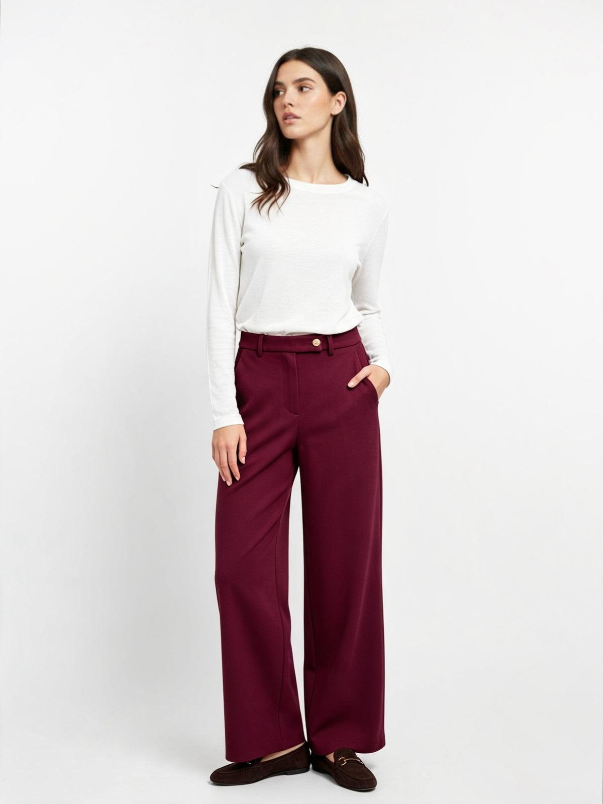 A woman modeling a white long-sleeve top and deep burgundy wide-leg trousers, paired with dark brown loafers, against a plain white studio background.
